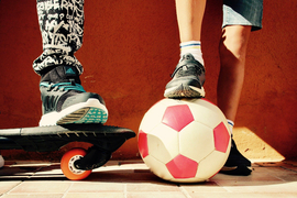 Beine von zwei Jungs mit Skateboard und Fußball