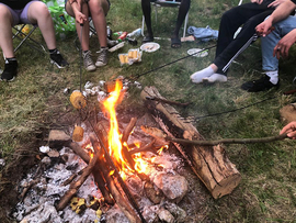 junge Leuten sitzen am Lagerfeuer und halten Stockbrot ins Feuer