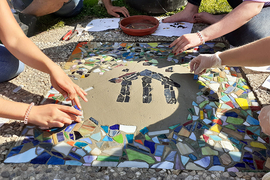 Jugendliche legen aus bunten Steinen ein Mosaik mit Don Bosco Logo